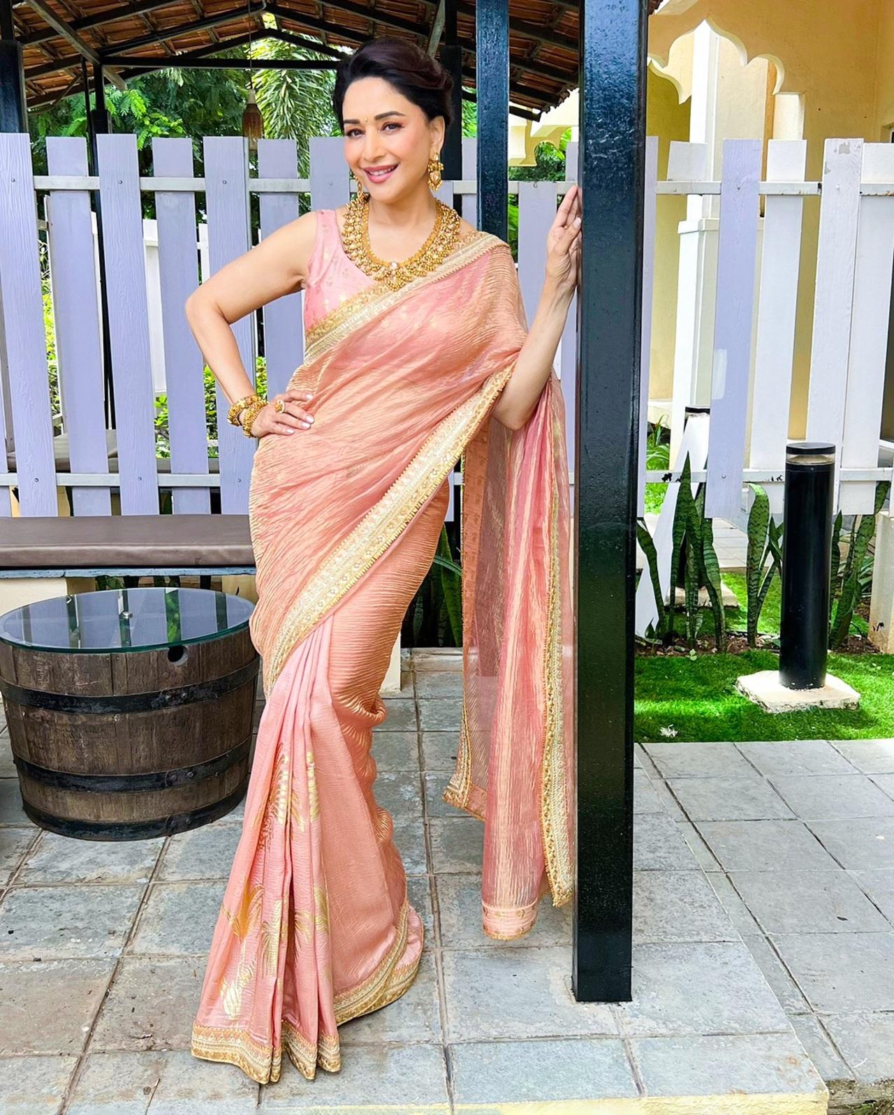 Madhuri Dixit exudes timeless grace in this pastel peach saree adorned with delicate golden border and patch work. This ensemble is a perfect choice for morning rituals, especially the Ganesh Sthapana or home pooja, where the need for subtlety, tradition, and comfort come together.